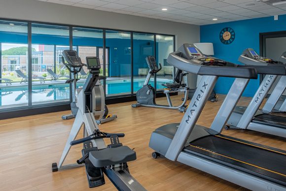 Salle de sport avec tapis de course, vitrée sur la piscine intérieure