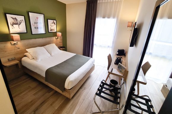 Chambre avec grand lit, mur vert et cadres au-dessus du lit