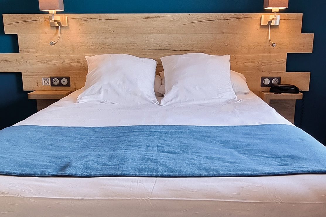 Chambre avec grand lit, tête de lit en bois et mur bleu canard