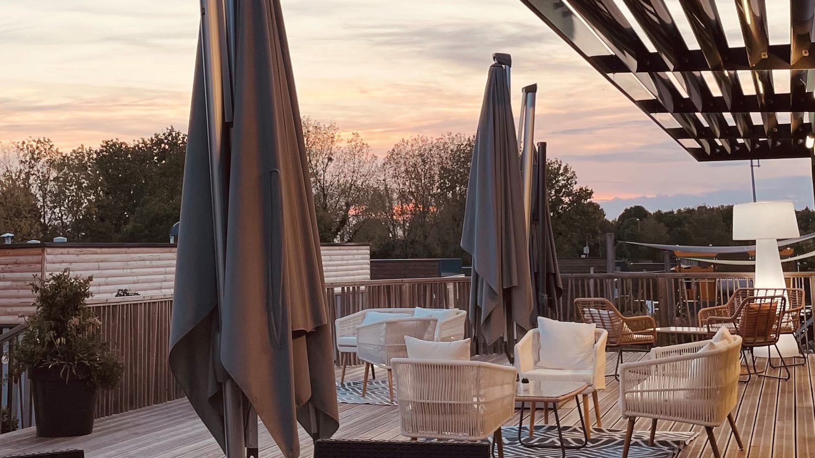Terrasse en bois au coucher du soleil, fauteuils blancs et parasols, arbres en arrière-plan