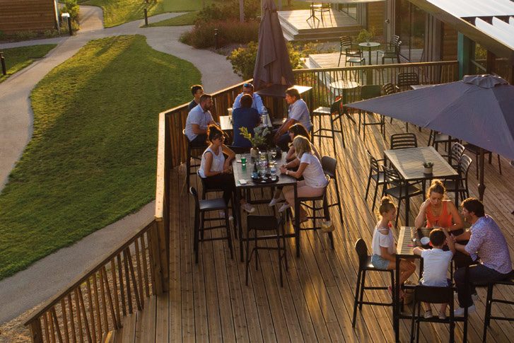 Terrasse en bois des lodges, entourée de pelouse, avec tables et parasols