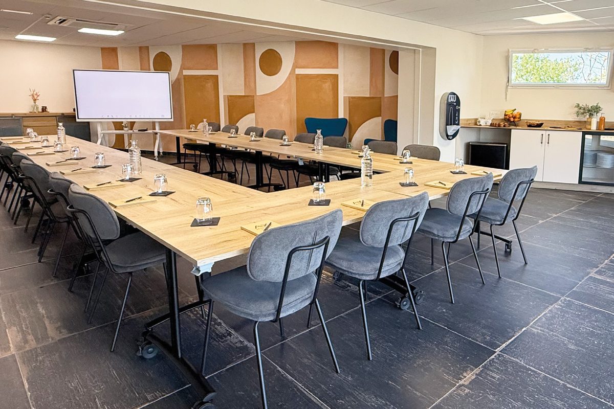 Salle de séminaire aménagée en U, écran au fond, murs décorés de formes douces orangées