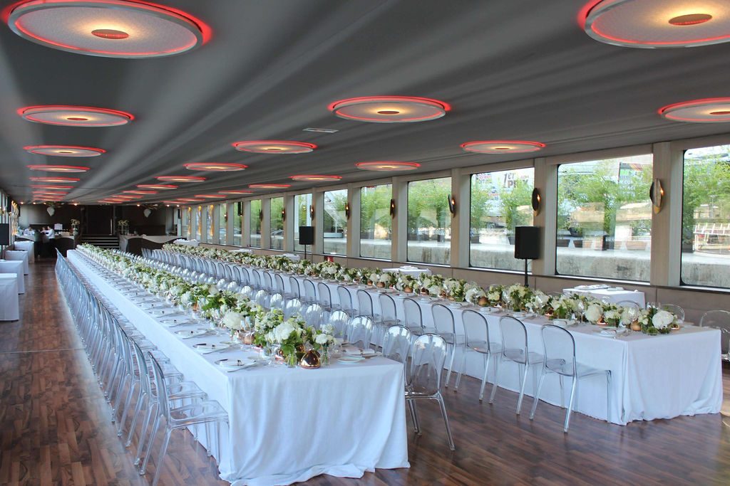 Longues tables de banquet dressées et fleuries sur toute la longueur de la salle
