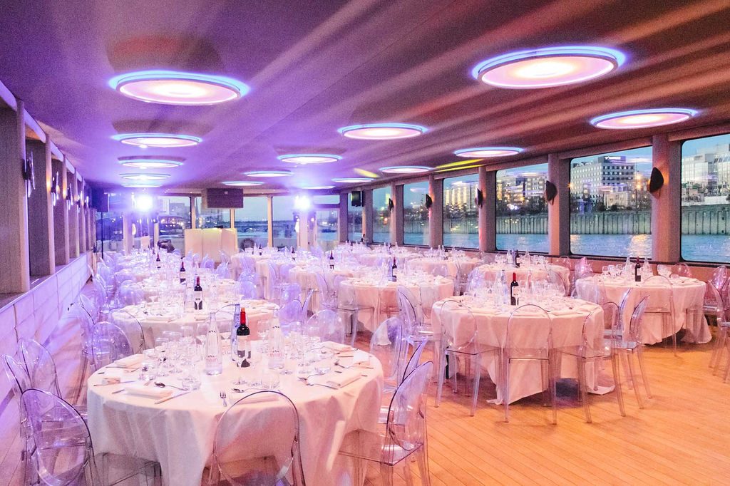 Tables rondes dressées de nappes blanches dans la grande salle, sous un éclairage violet