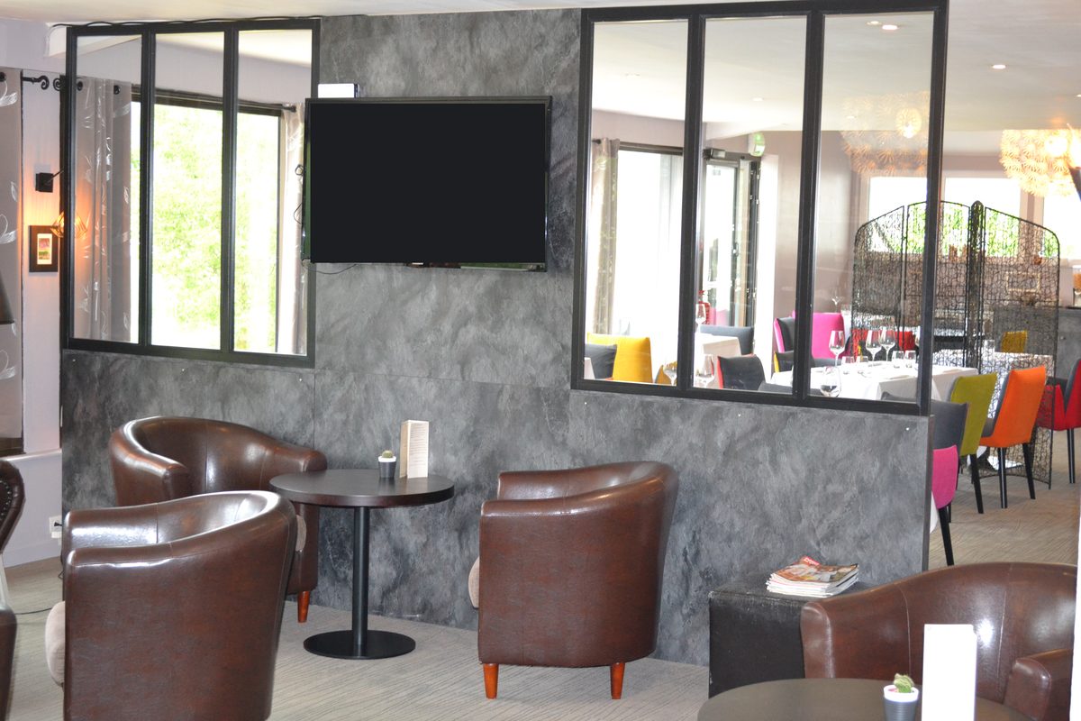 Le bar lounge, fauteuils club en cuir, verrière ouvrant sur la salle du restaurant aux chaises colorées