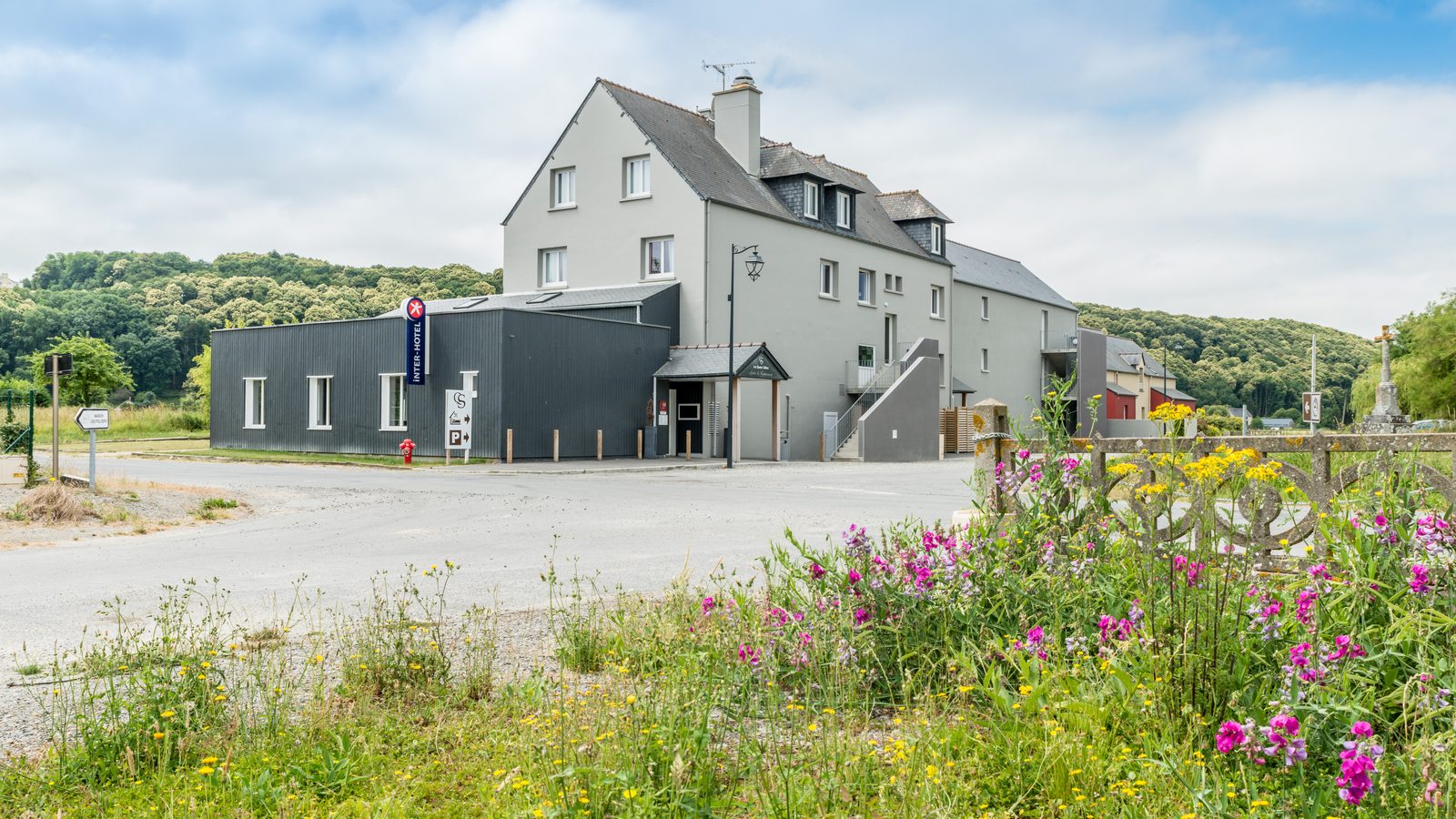 Façade de l'hôtel Les Quatre Salines, bâtisse claire aux toits d'ardoise, fleurs sauvages au premier plan