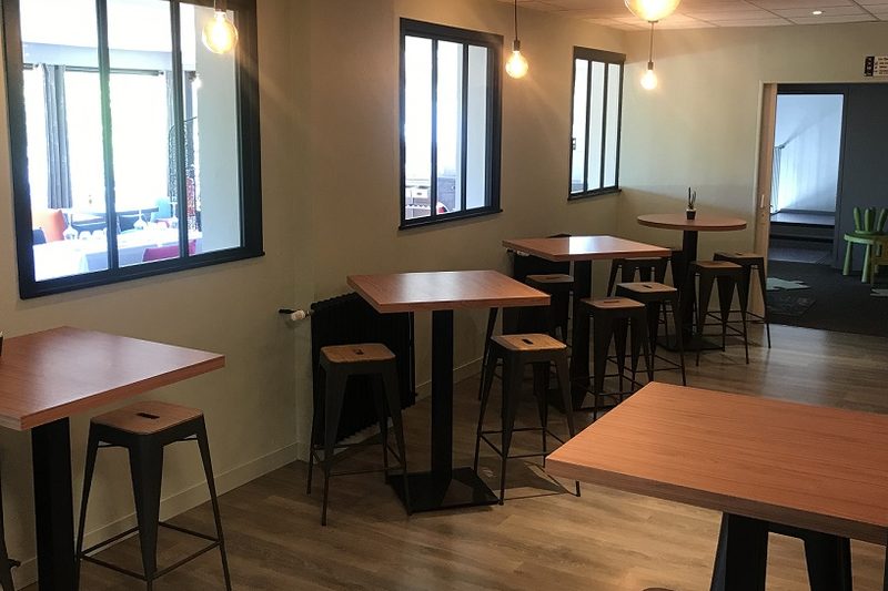 Espace pub avec tables hautes en bois et tabourets