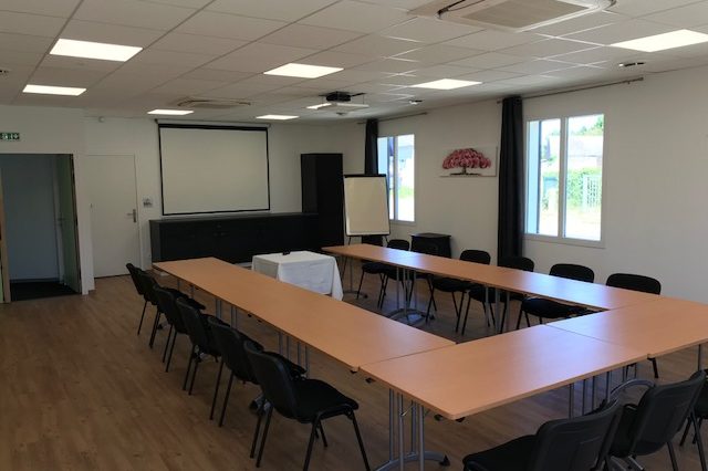 Salle de séminaire installée en U, chaises noires, écran de projection et paperboard au fond