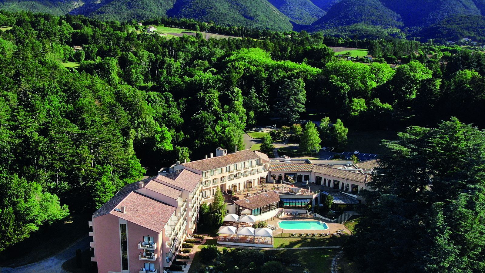 Vue aérienne du domaine Les Sources de Dieulefit, ses bâtiments aux toits de tuiles et sa piscine, au milieu de la forêt