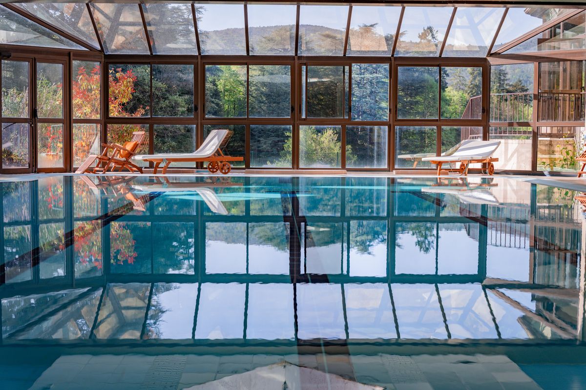 Piscine intérieure sous une verrière ouverte sur la forêt