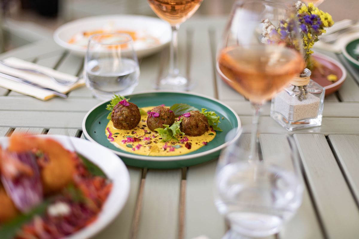 Assiettes colorées et verres de rosé sur une table en bois en extérieur