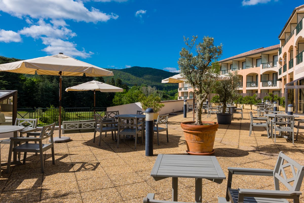 Grande terrasse avec parasols, oliviers en pot et vue sur les montagnes