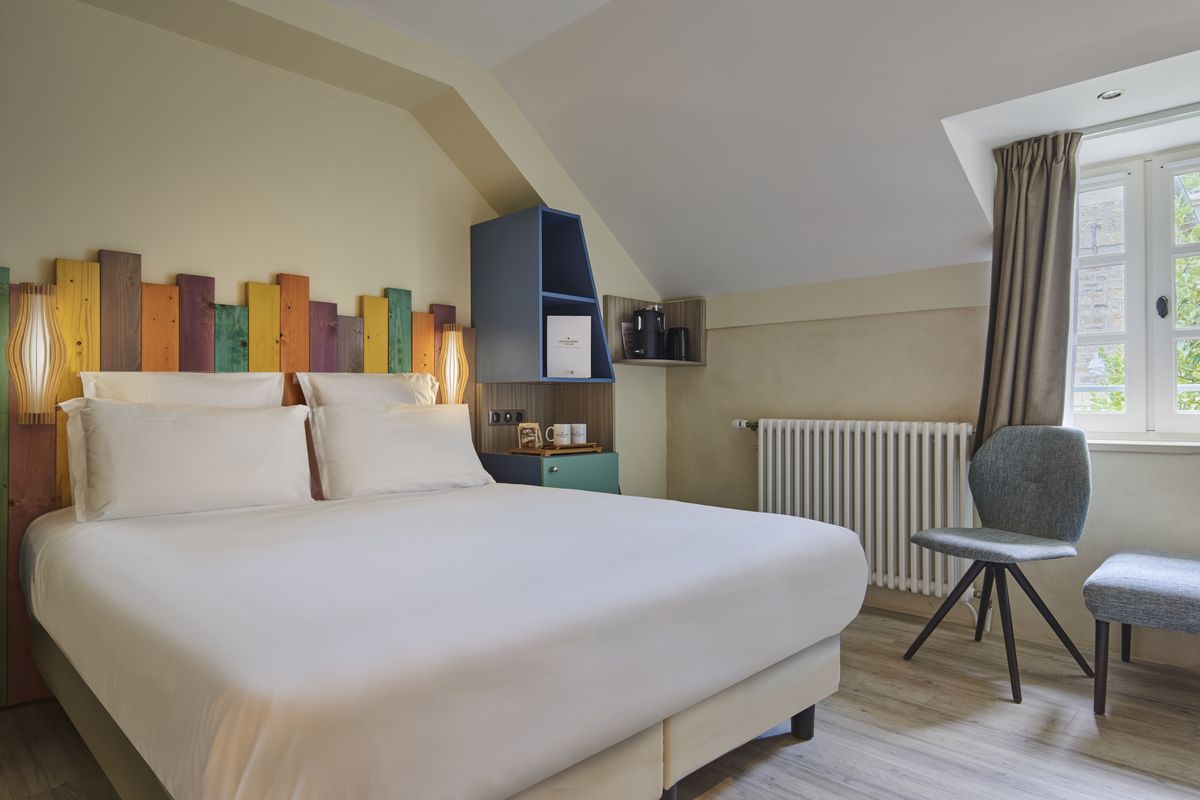 Chambre double claire avec tête de lit colorée et fenêtre mansardée
