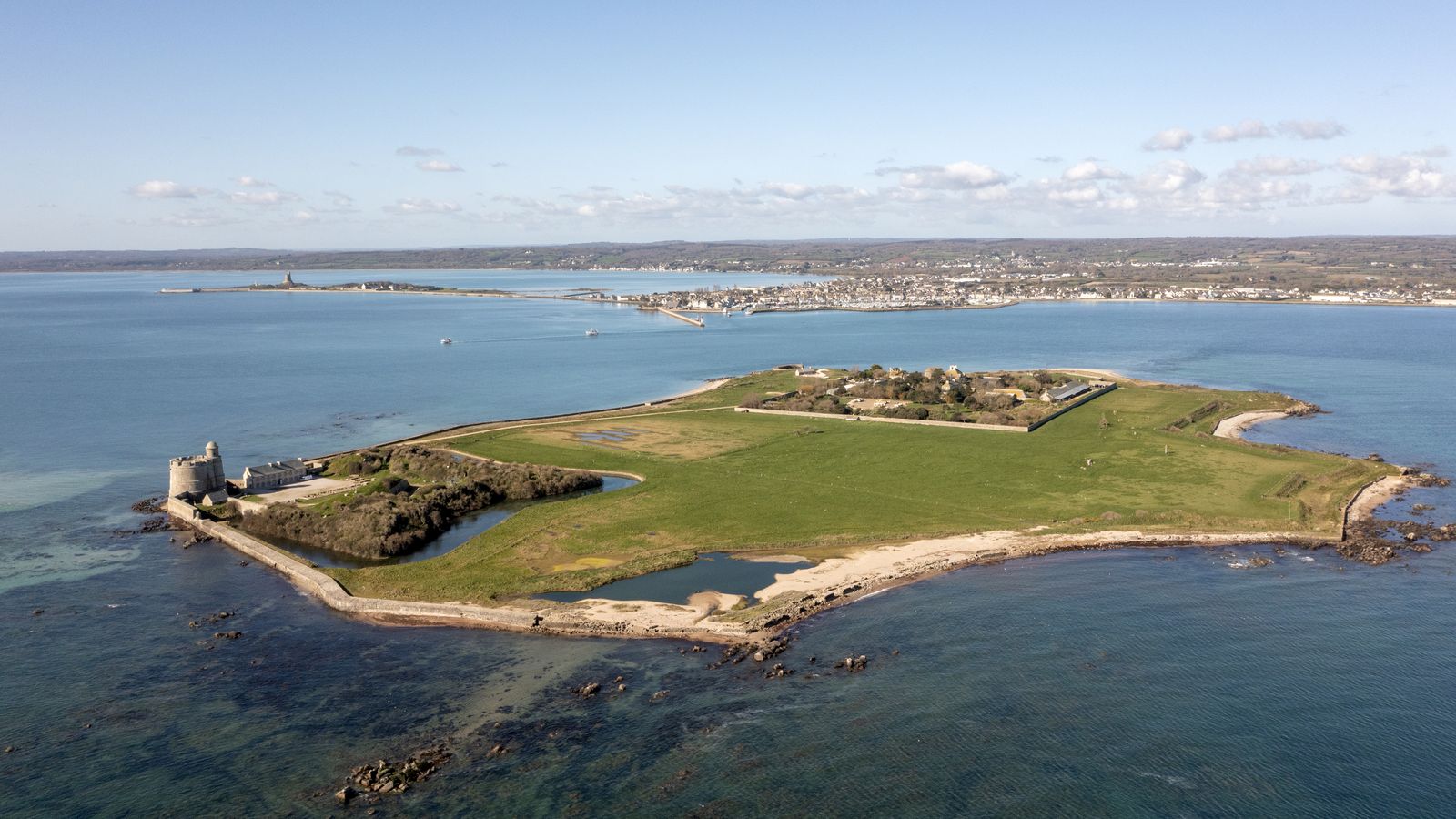 Vue aérienne de l'île Tatihou entourée de la mer, avec la côte de Saint-Vaast-la-Hougue en arrière-plan