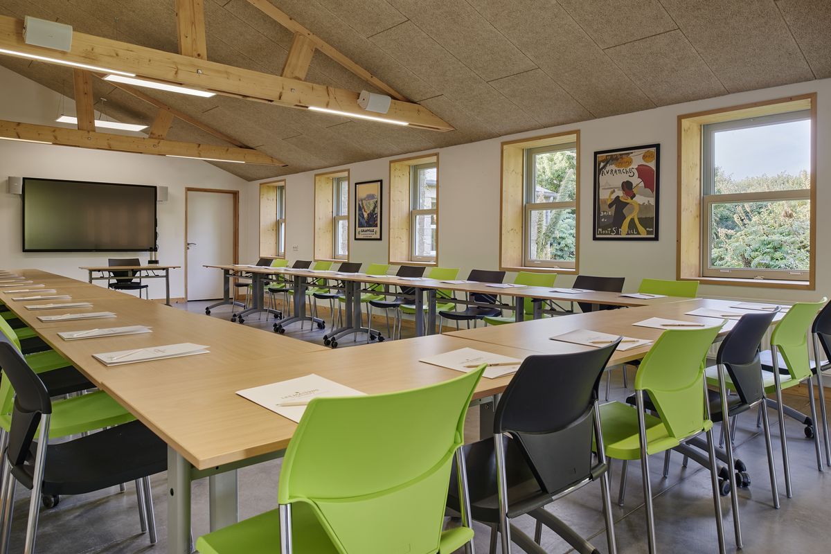Salle Calicocots, charpente apparente, tables en U et chaises vertes
