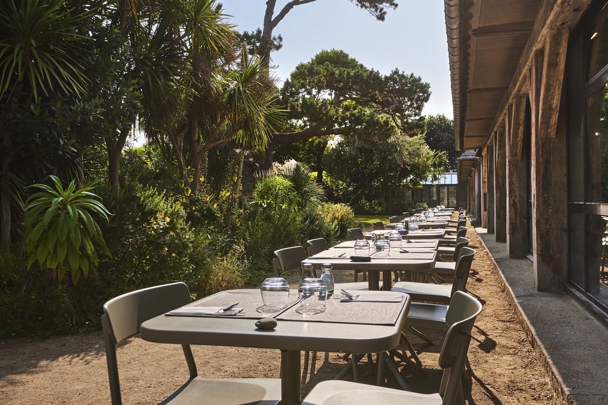 Terrasse du restaurant Le Carré le long du bâtiment, tables dressées sous les arbres